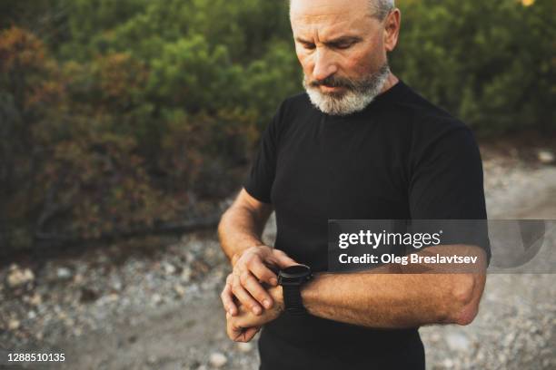 athletic senior runner start training on fitness tracker or smart watch. trail running and active lifestyle concept. - fitness armband stockfoto's en -beelden