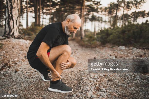 calf muscle injury on running outdoors. senior man holding knee by hands and suffering with pain. sprain ligament or periosteum problem. - sehnenscheidenentzündung stock-fotos und bilder