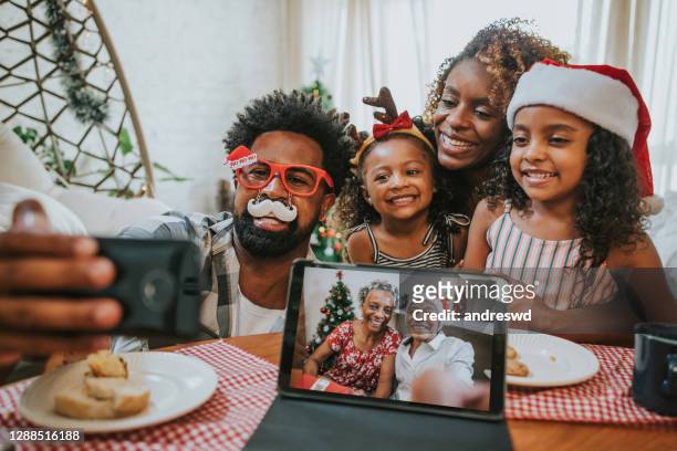 duas gerações de família celebrando o natal em casa e videoconferência com os avós, mantendo distância social - papa noel - fotografias e filmes do acervo