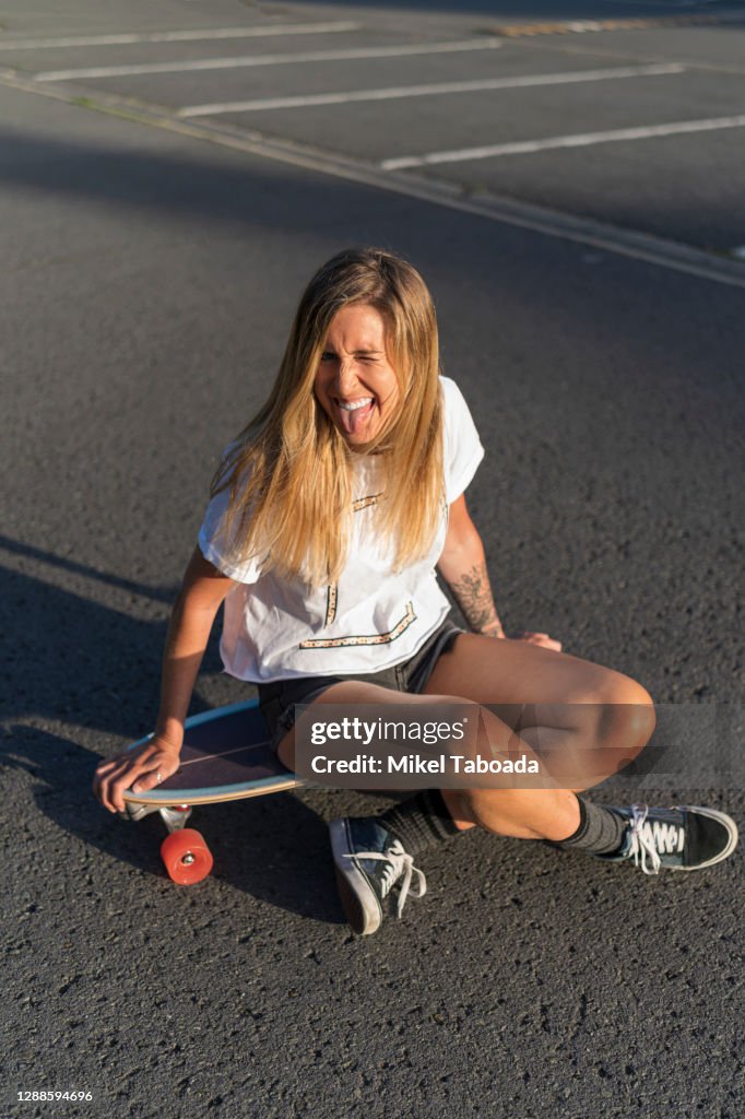 Happy blonde woman sitting on skateboard against sunset