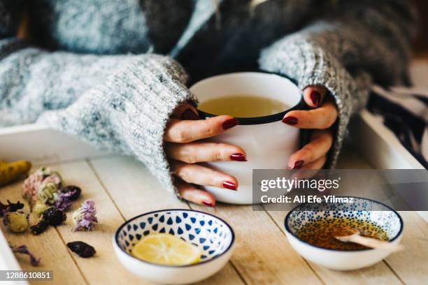 a female model is drinking herbal tea for flu, she is pouring herbal tea into a white enamel cup - tisana foto e immagini stock