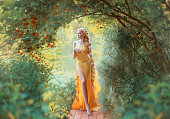 Beautiful young blond woman with very long hair that is braided. The girl is dressed in a seductive yellow dress with a slit on the leg. Fashion model posing against the backdrop of an autumn garden.