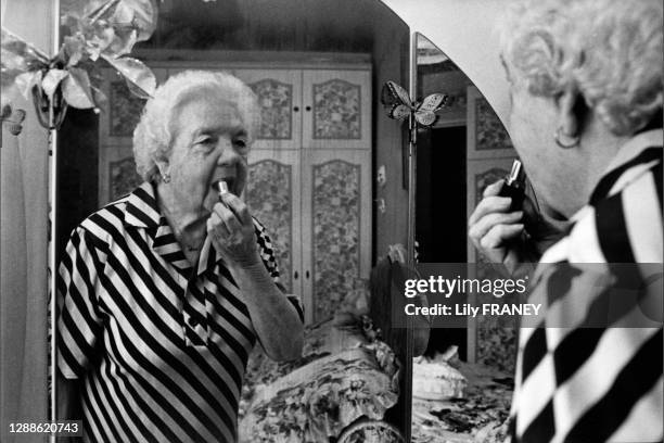 Femme retraitée se mettant du rouge à lèvres devant son miroir, Vitry-sur-Seine, Val-de-Marne France.