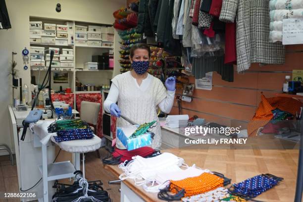 Retoucheuse confectionnant des masques et respectant la distanciation sociale à l'aide d'une barre et d'une boite pour donner aux clients durant le...