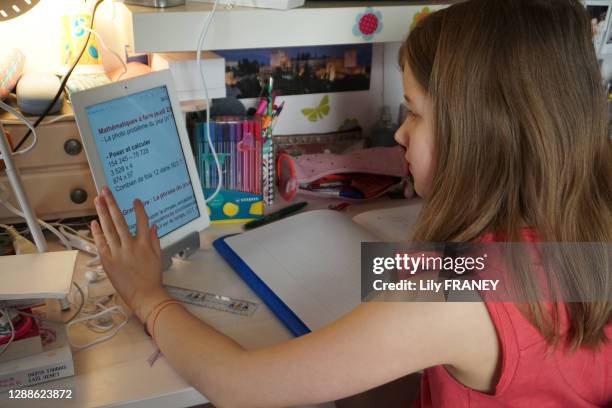 Classe à la maison, écolière en CM1 devant son bureau regardant sur sa tablette tactile son devoir de mathématiques à faire à distance, continuité...