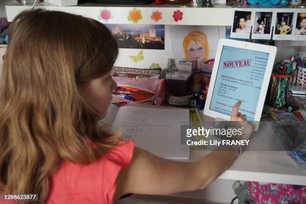 Classe à la maison, Ecolière en CM1 devant son bureau regardant sur sa tablette avec écran tactile son devoir de mathématique à faire à distance,...