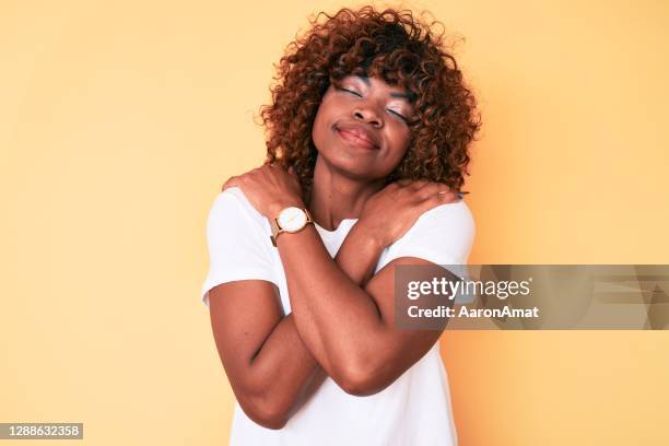 Young african american woman wearing casual white t shirt hugging oneself happy and positive, smiling confident. self love and self care