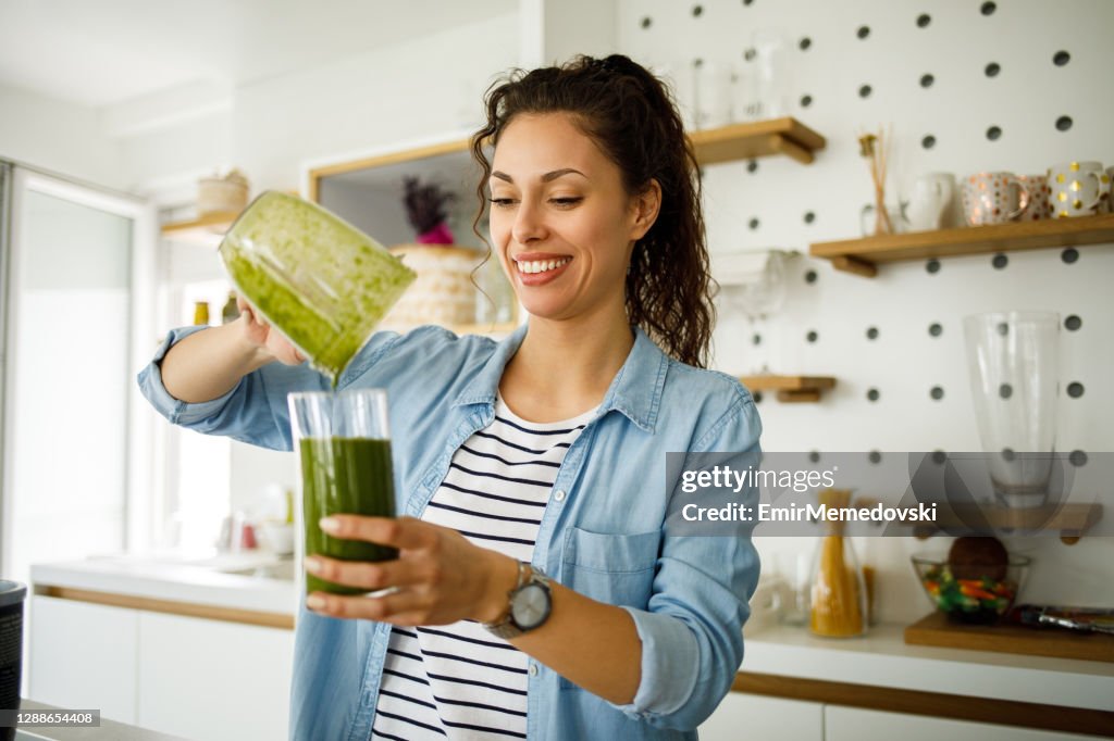 Junge Frau bereitet einen grünen Smoothie zu Hause