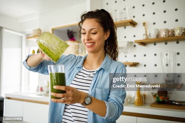 giovane donna che prepara un frullato verde a casa - juice foto e immagini stock