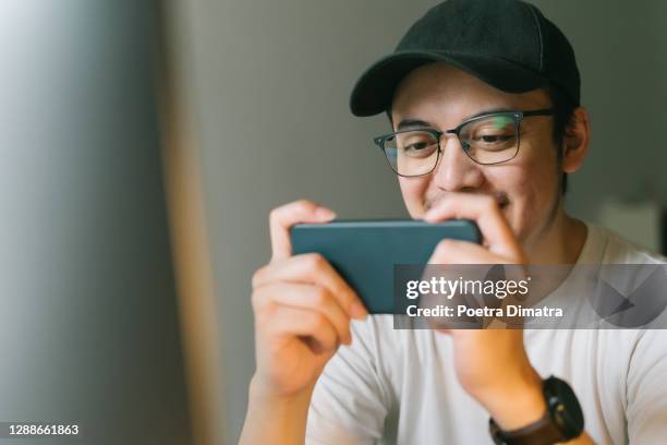 asian young man excited playing mobile game on his smartphone - mobile game stock pictures, royalty-free photos & images