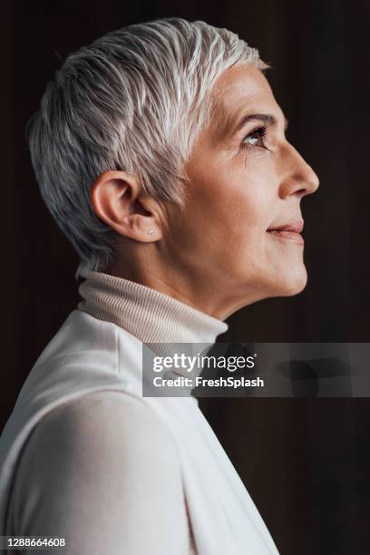 ritratto laterale di un'elegante donna anziana con i capelli grigi corti che indossa un elegante dolcevita bianco (sfondo scuro; contrasto) - profilo vista laterale foto e immagini stock