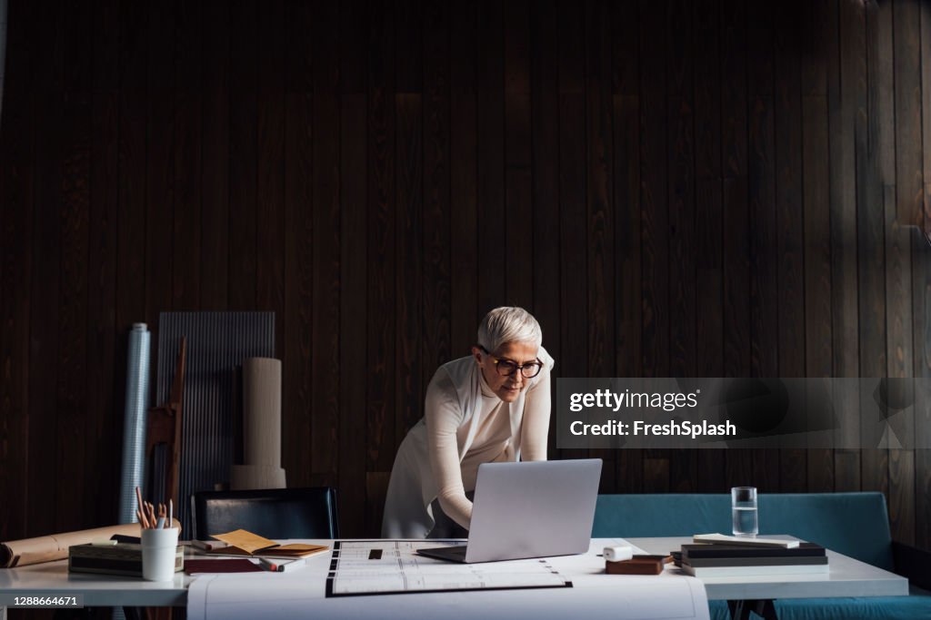 Designer Maduro Experiente trabalhando em um grande novo projeto e usando seu Laptop PC em seu Home Studio (Fundo Escuro)