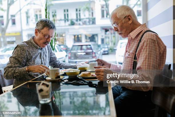 mature gay couple sitting down for breakfast at hotel together - senior men eating stock pictures, royalty-free photos & images