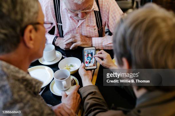 Woman Sharing Pictures On Smartphone With Family During Breakfast