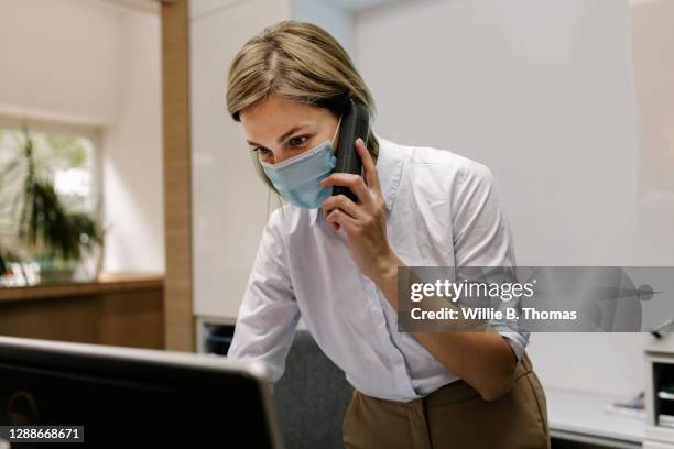 hotel receptionist talking on phone while wearing face mask - businesswoman mask stock pictures, royalty-free photos & images