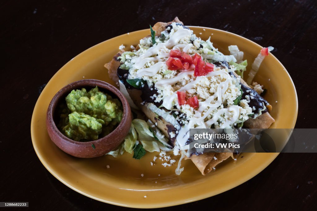 Tacos fritos, or crispy fried Oaxacan tacos stuffed with chicken, covered with queso fresco and served with guacamole on the side. Oaxaca, Mexico. Also known as tacos dorados, taquitos, or flautas. Near Oaxaca, Mexico.