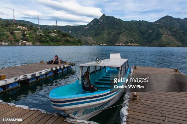 Passenger waits on a boat taxi at the dock in San Pedro la Laguna, Guatemala. A backpacking tourist relaxes on the dock. Lake Atitlan and the Nariz...