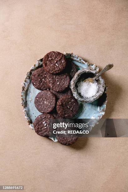 Homemade dark chocolate salted brownies cookies with salt flakes in blue ceramic plate over brown texture background. Flat lay, space.