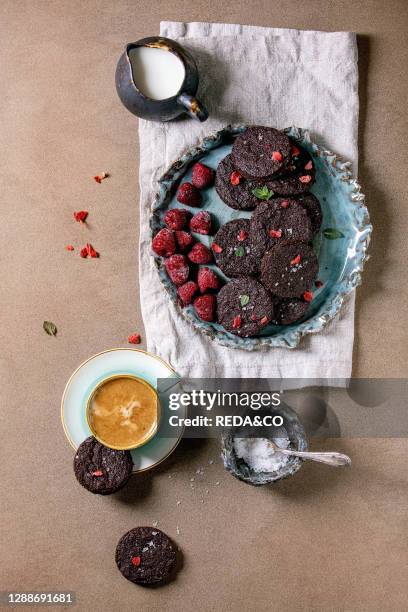 Homemade dark chocolate salted brownies cookies decorated by dry and fresh raspberries, served with salt flakes, berries, mint, milk and cup of...