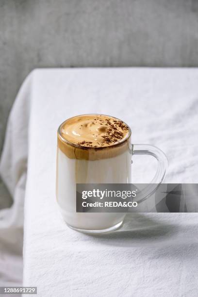 Dalgona frothy coffee trend korean drink milk latte with coffee foam in glass mug, decorated by ground coffee on white cotton table cloth.