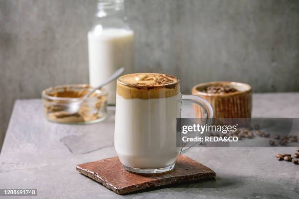 Dalgona frothy coffee trend korean drink milk latte with coffee foam in glass mug, decorated by ground coffee on gray texture table. Ingredients...