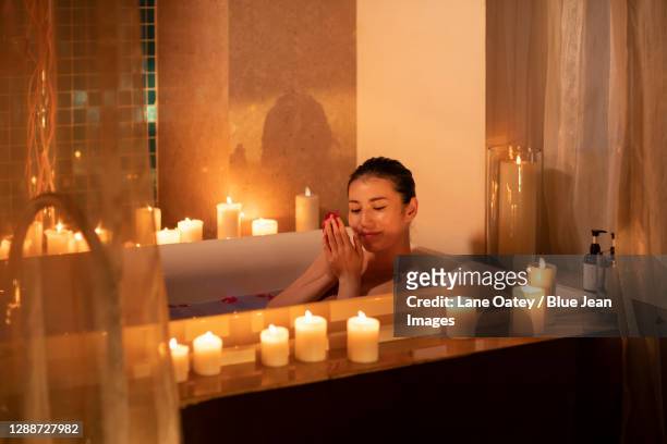 beautiful young woman in bathtub with rose petals - kerzenschein stock-fotos und bilder