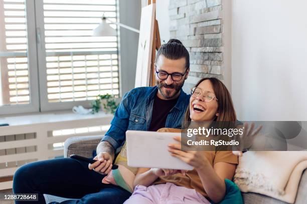 happy, young couple having fun online while relaxing on the sofa - young couple watching tv stock pictures, royalty-free photos & images