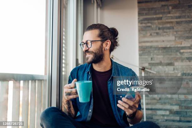 junger mann entspannt zu hause mit kaffee und mit dem smartphone - homme hipster stock-fotos und bilder