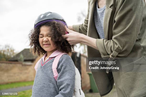 colegiala gruñendo mientras su madre se pone el casco de ciclismo - demasiado pequeño fotografías e imágenes de stock