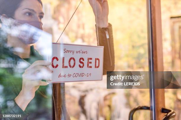 a young woman puts a sign reading "closed" on the door of her store - 店の看板 ストックフォトと画像