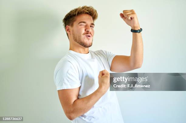 man making triumph gesture in front of white wall - mann siegerpose stock-fotos und bilder