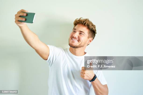 man taking a selfie with mobile phone in front of white wall - taking selfie white background stockfoto's en -beelden