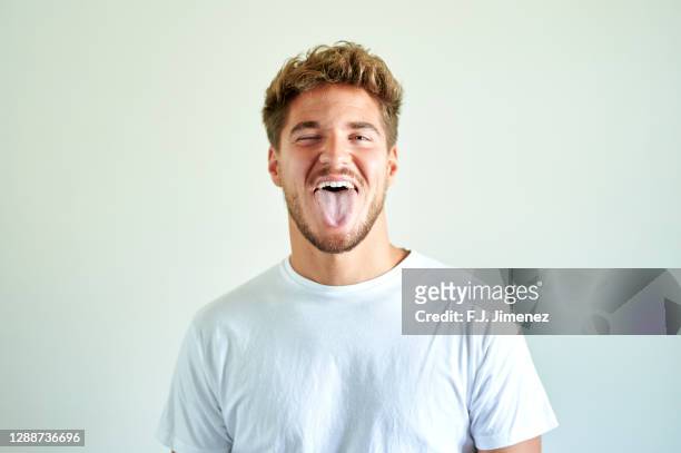 portrait of man sticking out tongue in front of white wall - sticking out tongue stock pictures, royalty-free photos & images