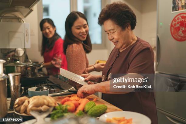 females from a multi-generation asian family in a kitchen during the preparation of reunion dinner - prosperity stock pictures, royalty-free photos & images