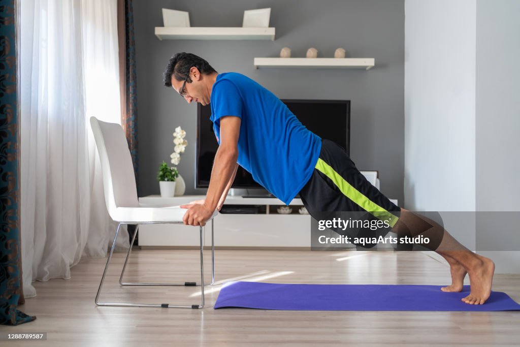 Joven atlética está haciendo ejercicio push up con silla en casa en su amplia sala de estar con interior moderno. Gimnasio en casa