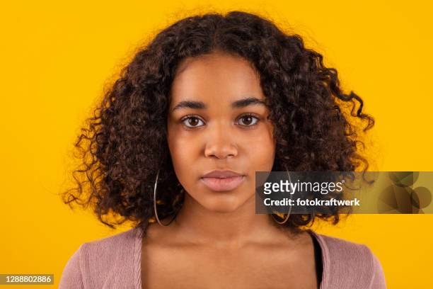 close-up portrait of young woman with curly brown hair against yellow background - curly brown hair stock pictures, royalty-free photos & images