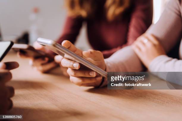 sección media de amigas usando teléfonos móviles en la mesa mientras están sentadas en café - social gathering fotografías e imágenes de stock