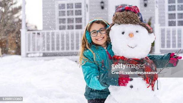 girl playing with a snowman in front of the house - snow man stock pictures, royalty-free photos & images