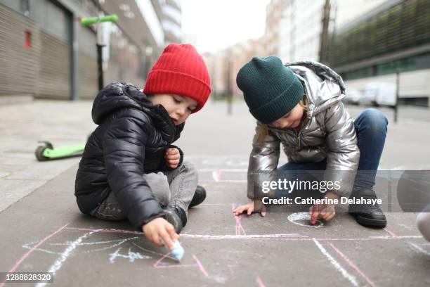 2 children drawing with a chalk stick in the street - paris hiver photos et images de collection