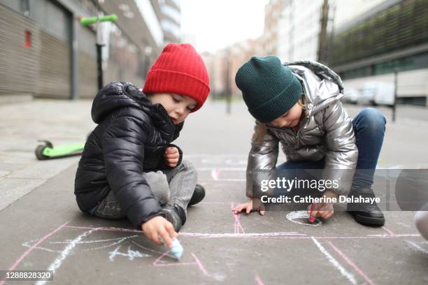 2 children drawing with a chalk stick in the street - family chalk drawing stock pictures, royalty-free photos & images