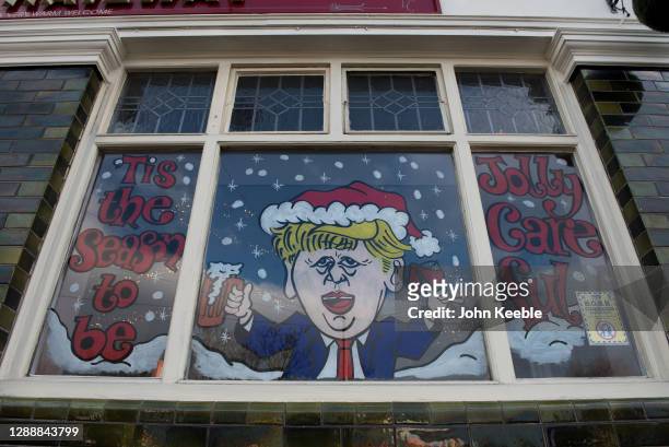 Humorous decorated window on The Railway pub showing a caricature of Prime Minister, Boris Johnson and the words "This the season to be jolly...