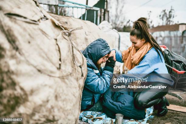 altruïstisch vrouwelijk verwarmend dakloos mannetje met jasje - homeless person stockfoto's en -beelden