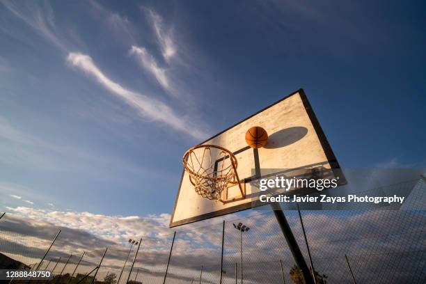 basketball goal and ball at sunset - basketball net stock-fotos und bilder