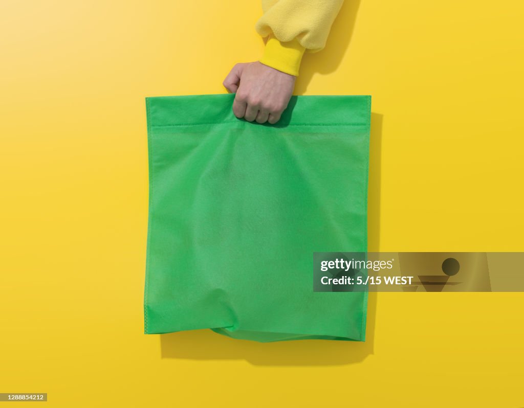 Hand hält grüne Baumwolltasche auf gelbem Hintergrund