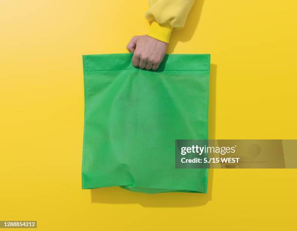 mano sostiene bolsa de algodón verde sobre fondo amarillo - bolso tote fotografías e imágenes de stock