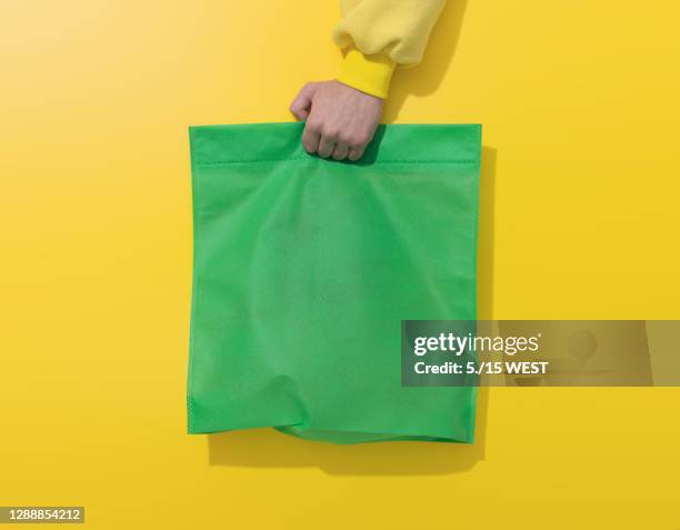 de hand houdt groene katoenen zak op gele achtergrond - herbruikbare tas stockfoto's en -beelden