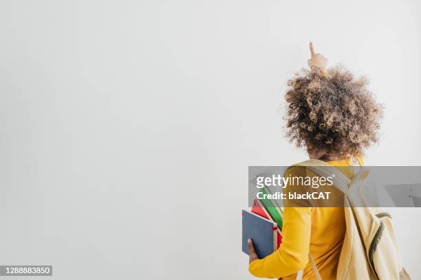 rückansicht eines afroamerikanischen niedlichen mädchens, das schulbücher hält und auf einen kopierraum zeigt - girl pointing stock-fotos und bilder