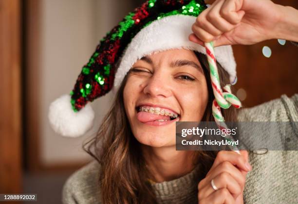 smiling woman in a santa hat making a face and holding candy canes - braces imagens e fotografias de stock