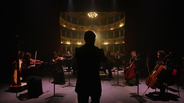 Cinematic shot of conductor directing symphony orchestra with performers playing violins, cello and trumpet