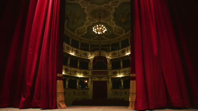 Cinematic shot of empty classic theatre with red velvet curtains opening stage with dramatic lighting